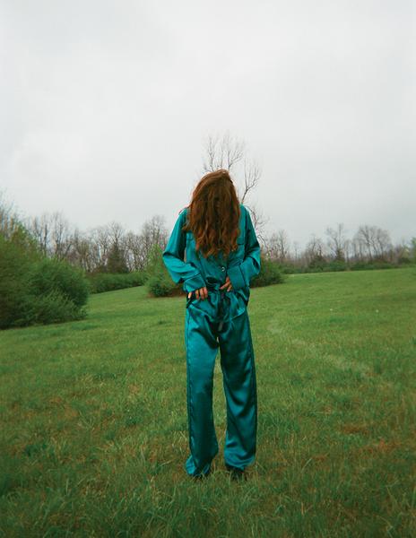 Woman in blue silk pajamas standing on a grassy field.