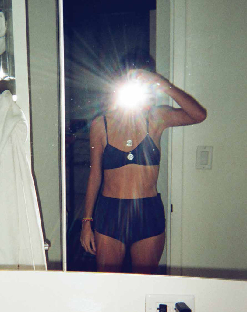 Woman in blue underwear and a blue bra taking a photo of herself in a mirror.