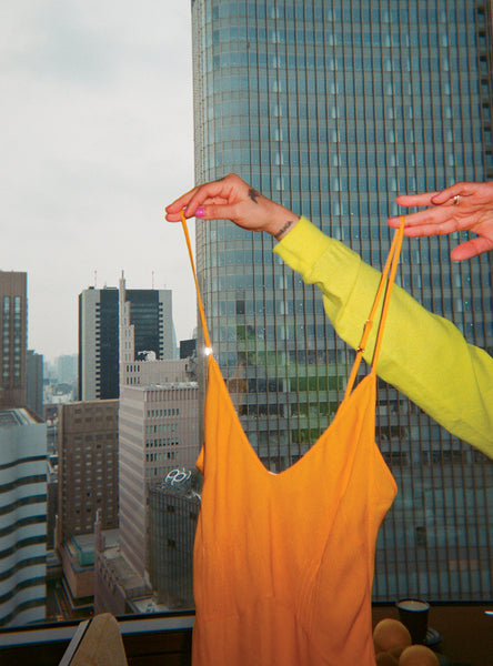 Woman holding an orange chemise over a view of a city.