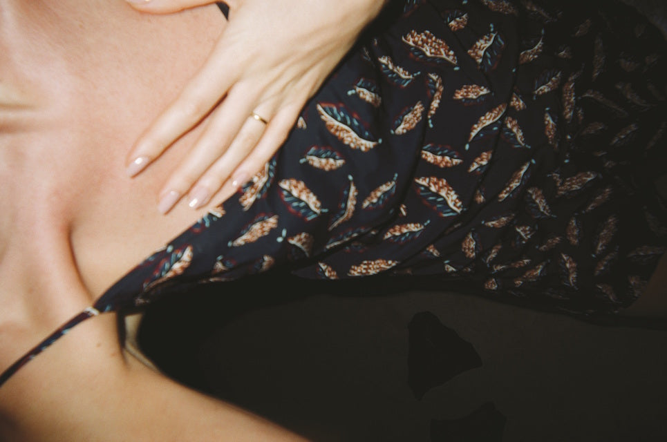 Up close photo of a woman in a black patterned dress holding her chest.