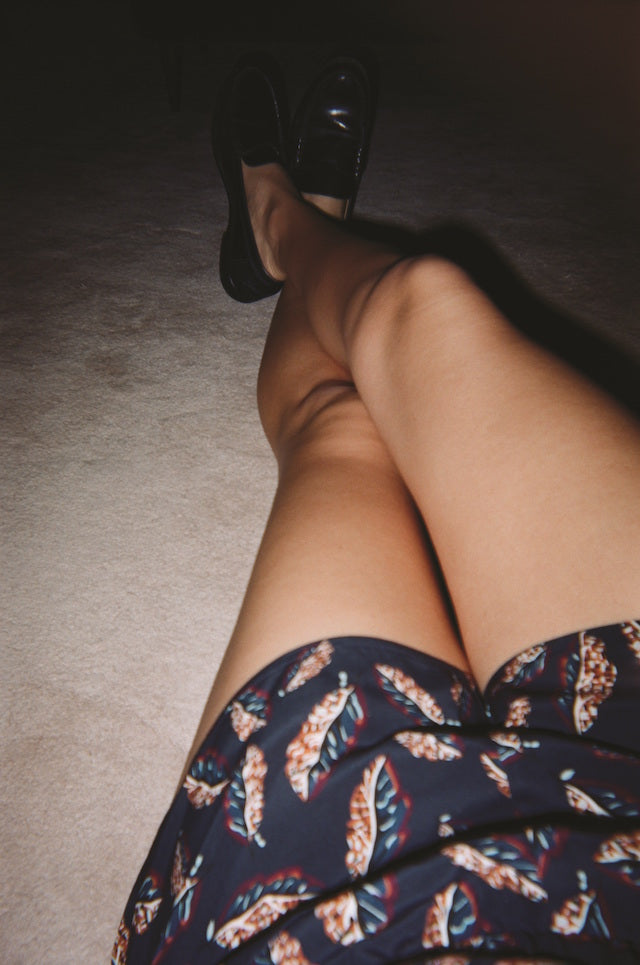 Woman's black printed leaf pajama shorts with a view of her legs in black shoes.