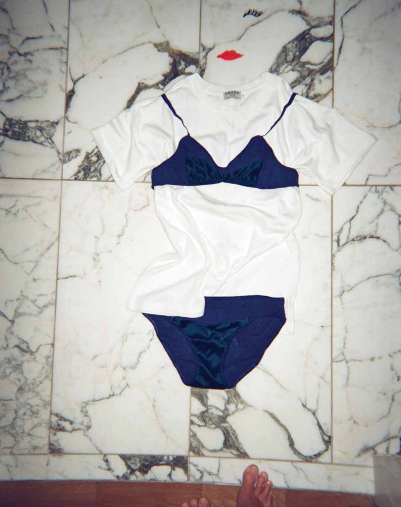 Blue underwear and a blue bra placed over a white T shirt on a marble floor.