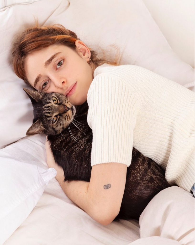 Woman in a white sweater holding onto her cat in bed.