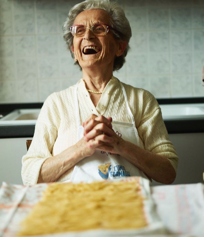 Older woman laughing with a plate of pasta.