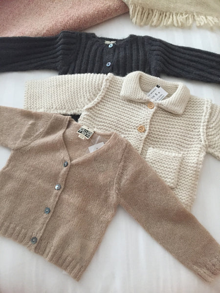 A black, white and beige baby sweater laid on a bed.