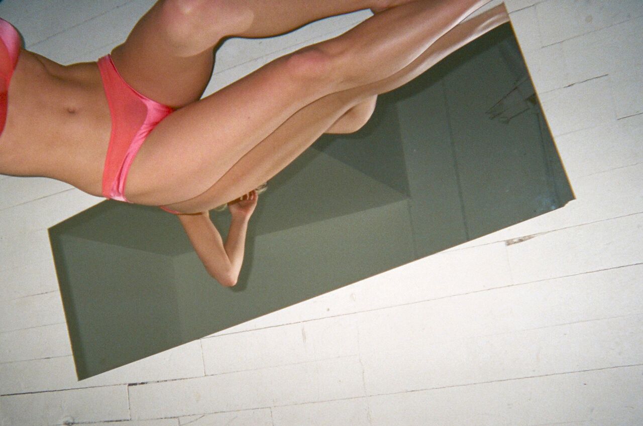 Bottom shot of a woman in pink underwear standing over a mirror.