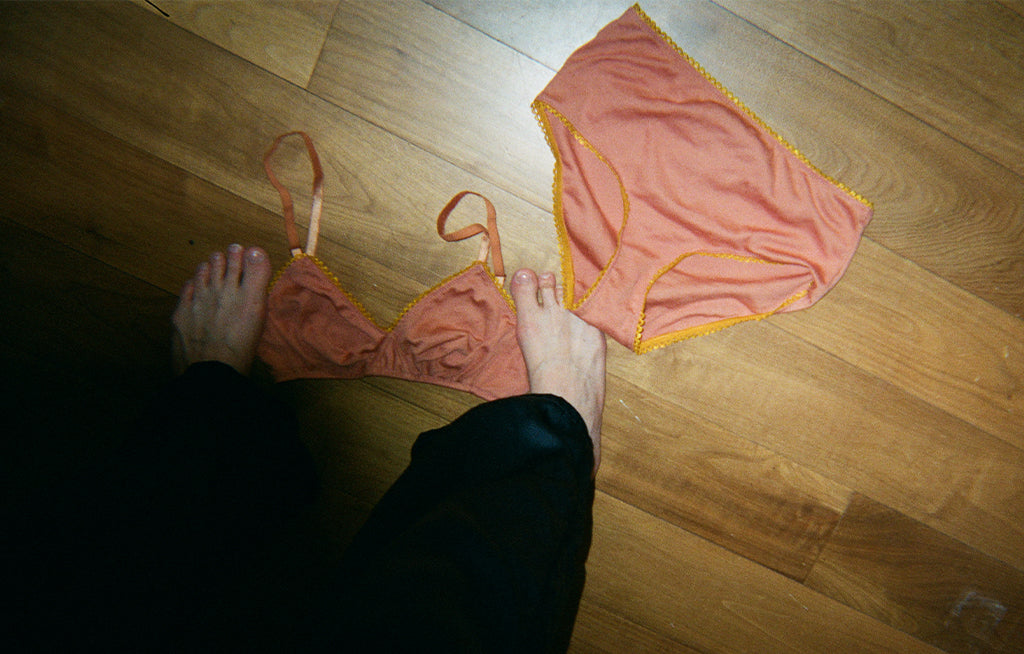 Feet stepping on a pink bra and underwear.