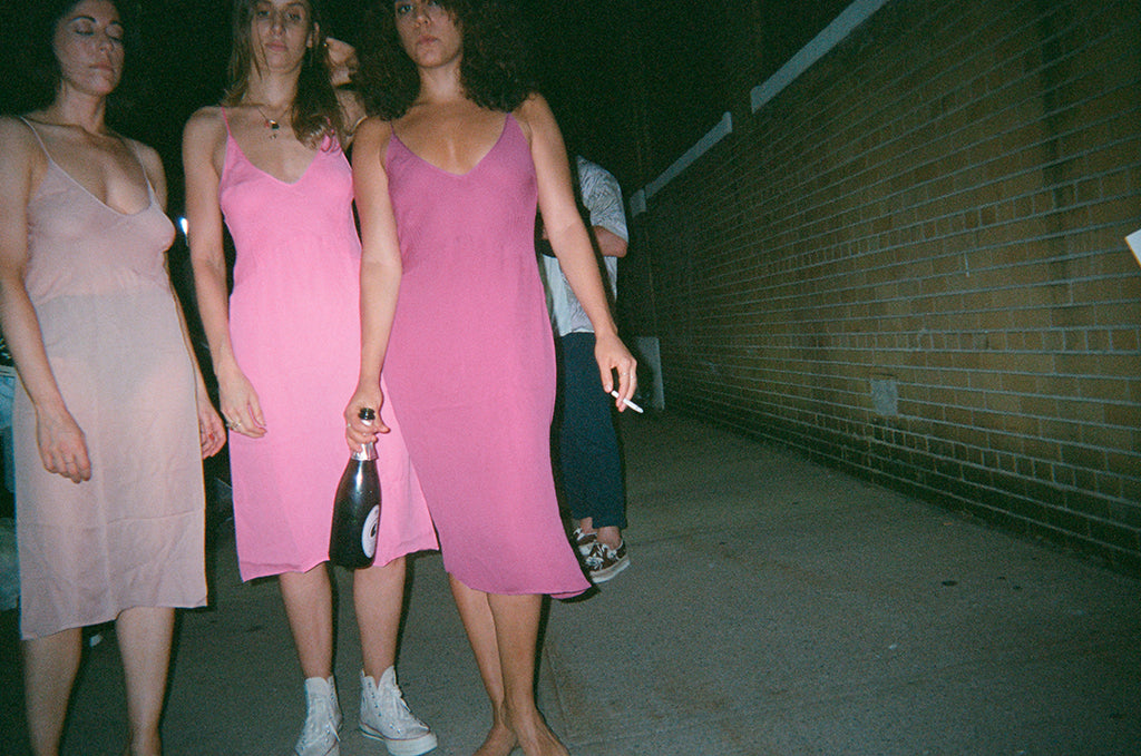 Three woman in pink slips standing with one holding a bottle of wine.