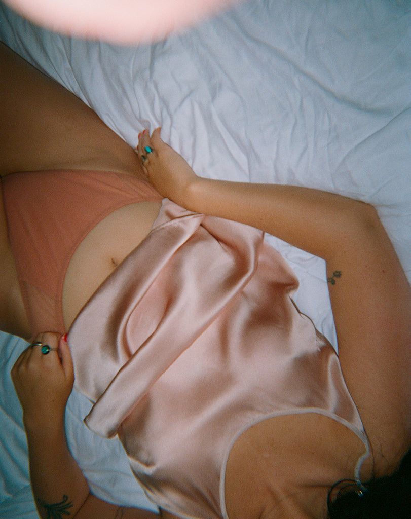 Woman in a pink chemise and tights laying on a bed.