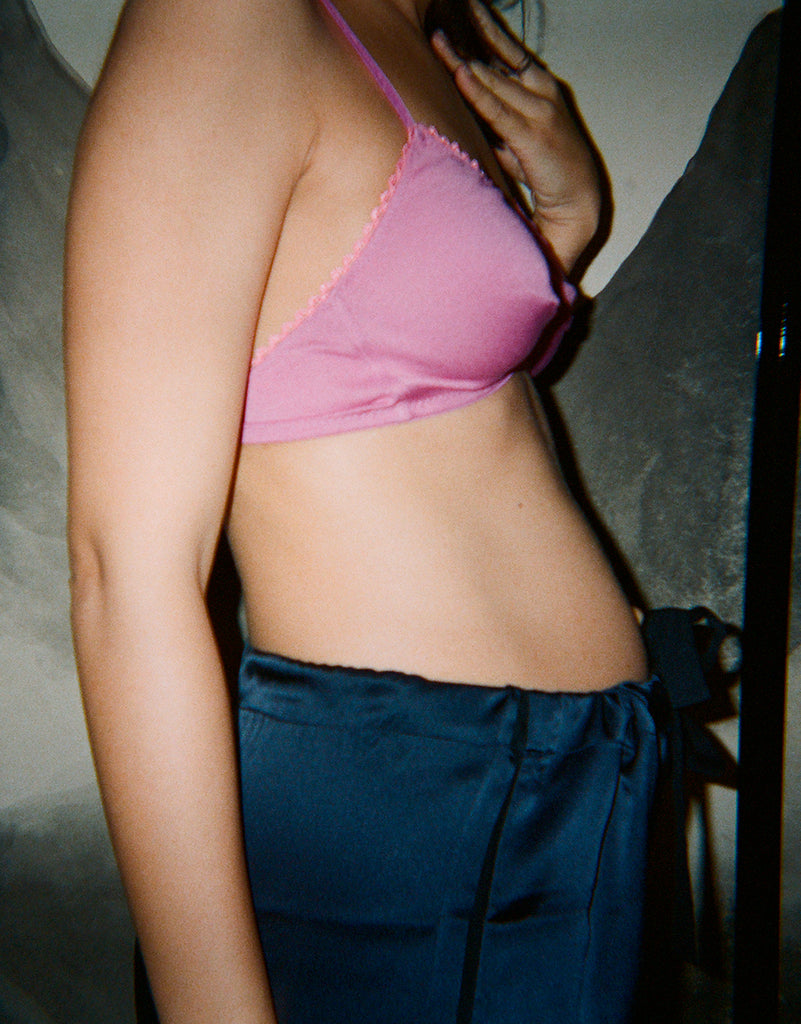 Side view of a woman's body in a pink bra and blue pajama pants.