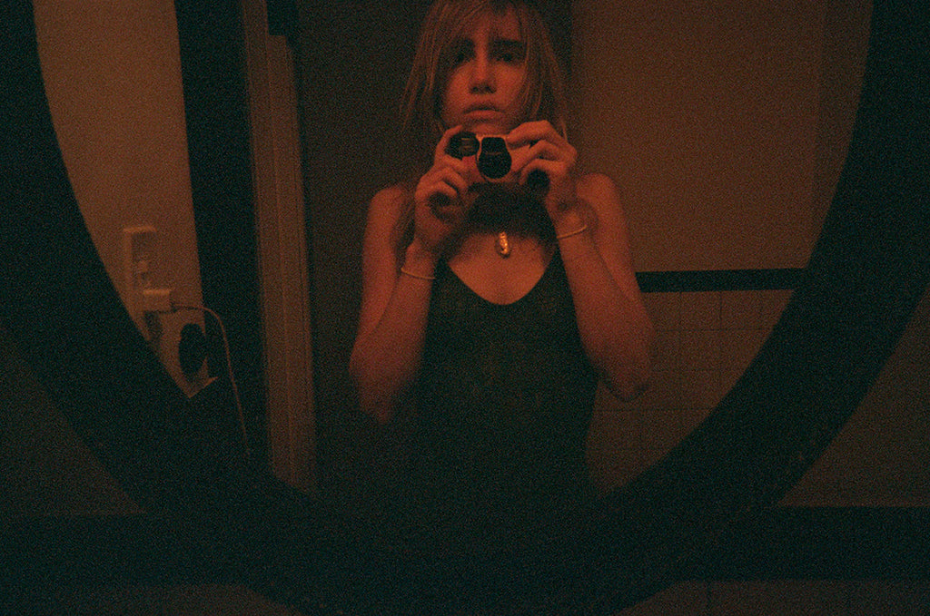Woman taking a photo of herself in a mirror in a black body suit.