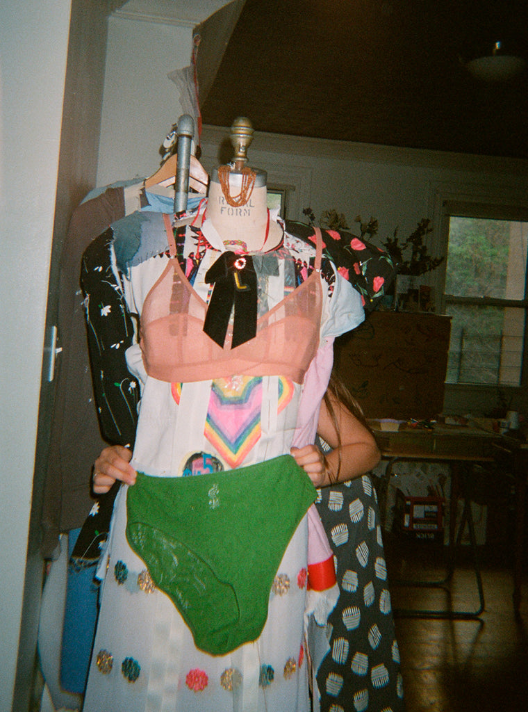 A pink bra and green underwear being held over multiple pieces of clothing.