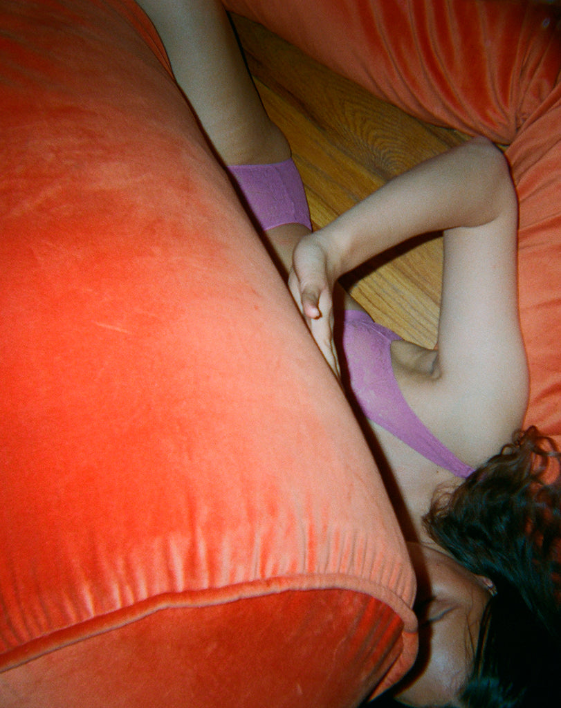 Woman in a purple bra and underwear under an orange couch.