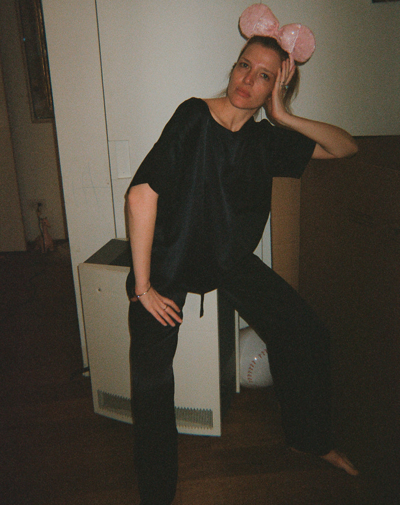 Woman in pink mouse ears and black shirt and pants sitting.