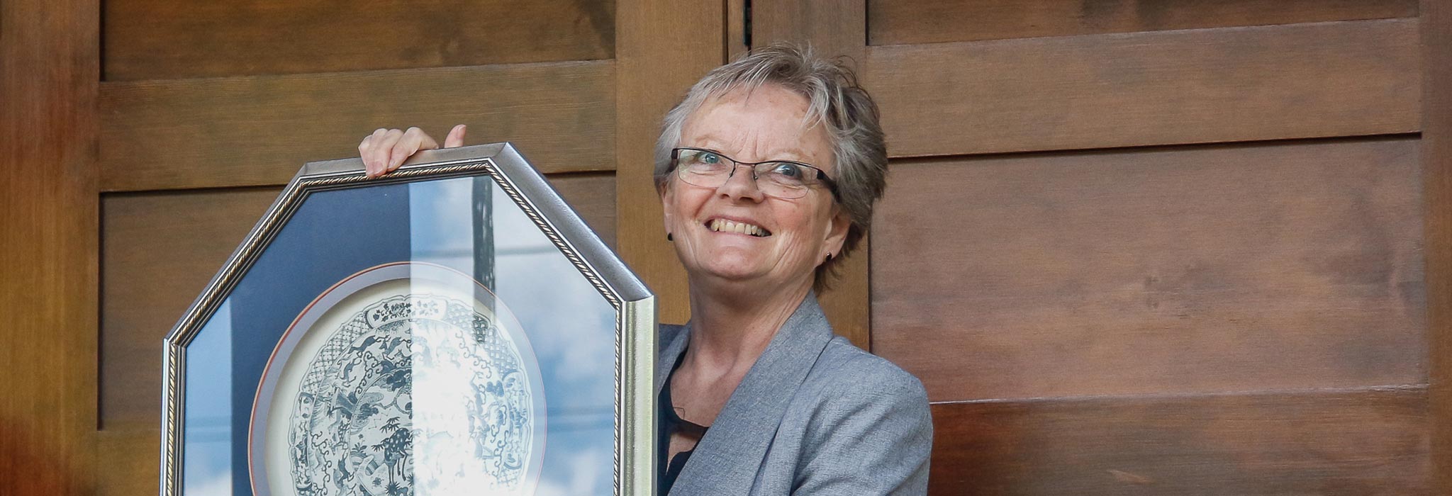 Lorna Fandrich holding a framed plate at the doors of the museum 