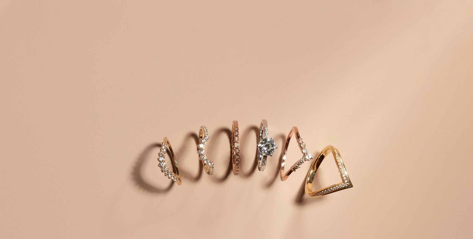 A cascade of wedding bands and an engagement rings on a pink background