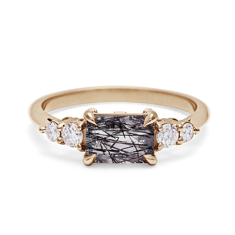 A ring with an emerald shaped black rutilated quartz center stone with two round white diamonds on either side set in yellow gold. 7