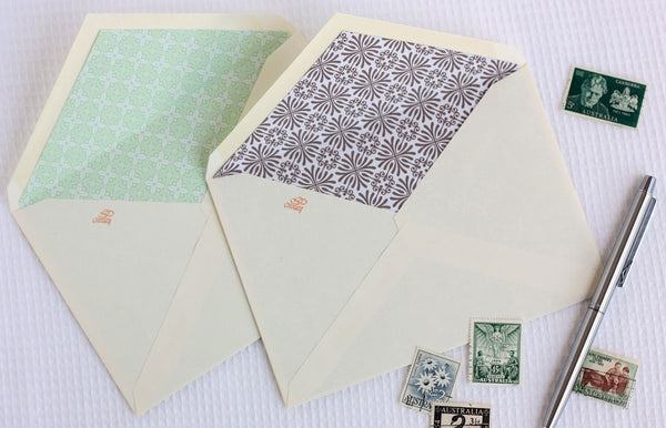 Lined envelopes next to stamps and pen