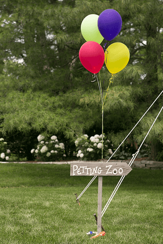 Sign with balloons attached reading Petting Zoo at barn wedding
