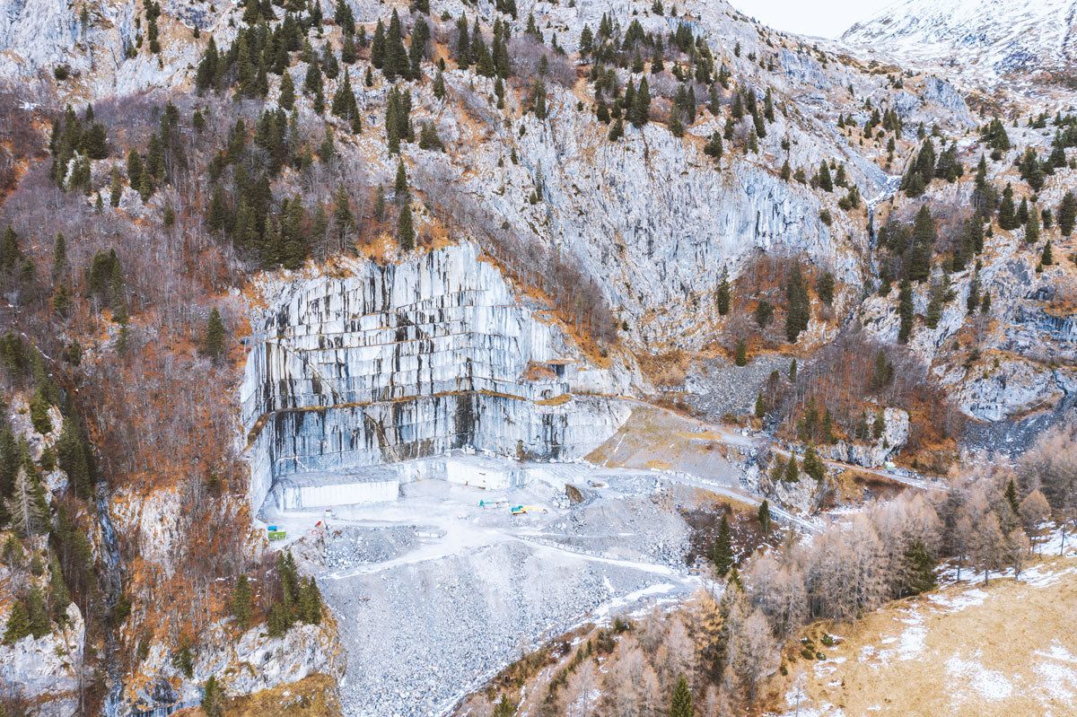 Isolated, solitary, at rest, the Grigio Carnico quarry in Udine emerges as an open-sky field, surrounded by the greenery of the Alpine forest. Its exterior walls, suggestive, show the different veining and color hues, revealing the passing of the years and the area’s geological evolution.