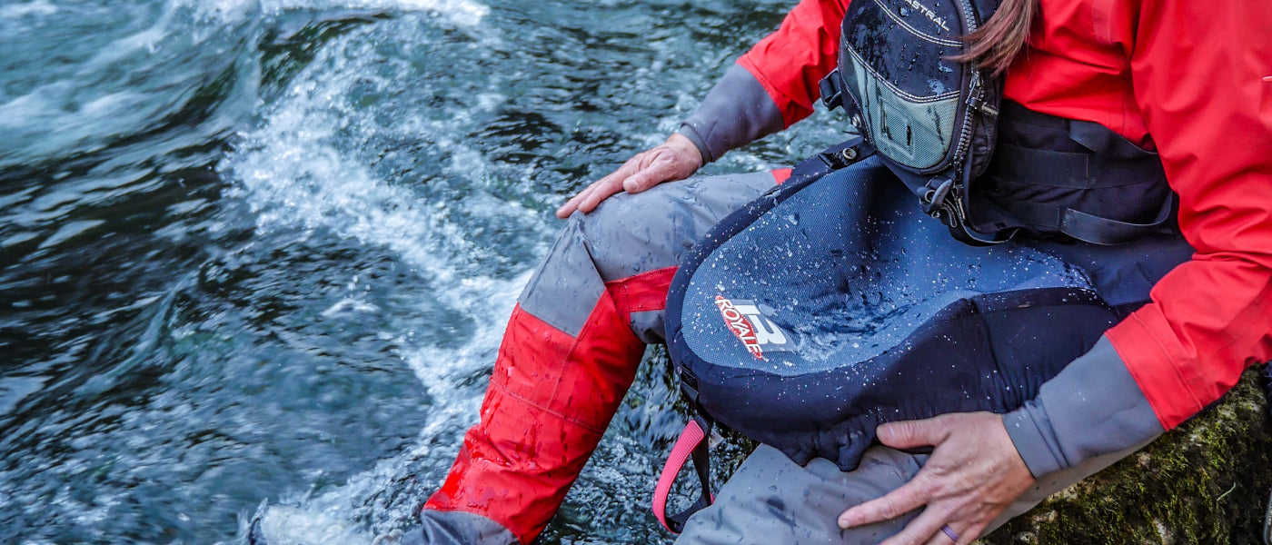 Kayaker sitting next to a river while wearing a dry suit and spray skirt