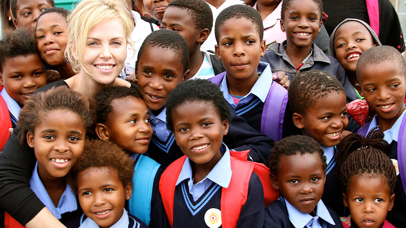 Charlize Theron smiles with a group of African children.