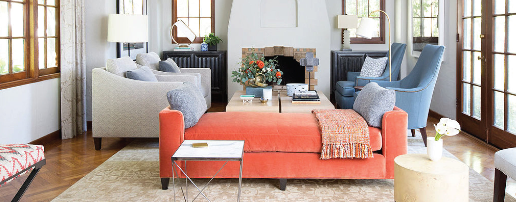 light filled living room interior featuring salmon colored daybed two grey lounge chair and two light blue club chairs in front of a fireplace