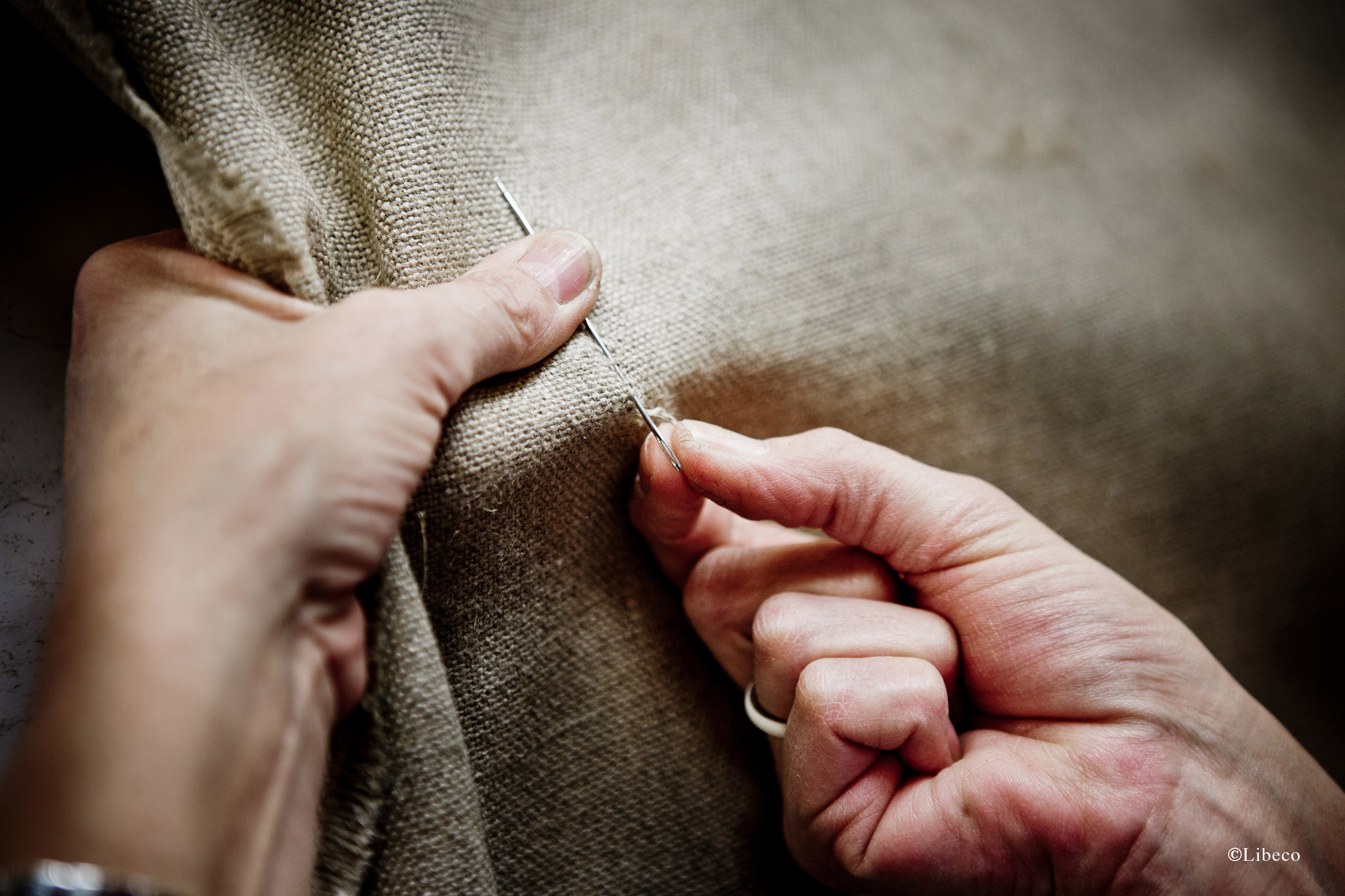 Hands threading a needle into linen cloth