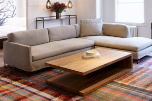 Molino Ash的所有ister沙发是一个右臂面向配置. 这是沙发套, 在一间白色的房间里，前面有一张大的木咖啡桌，桌子上放着鲜艳的颜色, 花纹的地毯.  