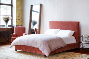  四月床在莱西法国玫瑰旁边的一把椅子，一个落地镜，和一边暗一边桌. 背景是一面白色的墙和一面带有一扇大窗户的砖墙.  
