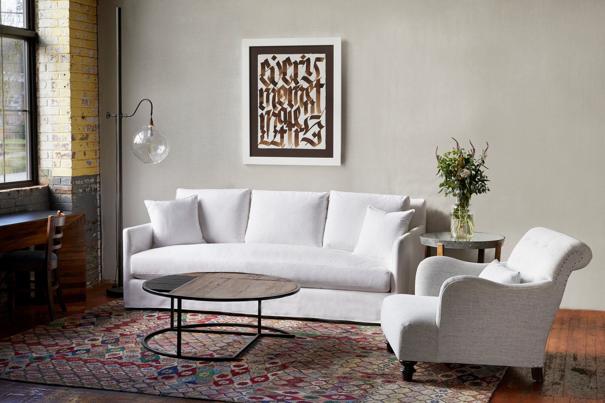  客厅设置大窗户. 白色的沙发，白色的金合欢椅和木制的咖啡桌. 沙发左边的落地灯和墙上的艺术品.  