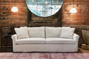  浅色的沙发在深色木墙前，有两个白色的吊灯和一个大的圆形镜子 