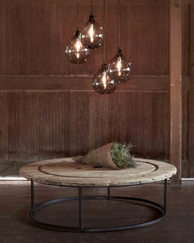 木制的圆形咖啡桌，四盏烟熏灯悬挂在咖啡桌上方. 背景是木墙，咖啡桌上放着一束鲜花. 