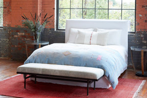  林肯长椅在Sakura Silver的白色软垫床的尽头. 床上是浅蓝色的被套.  床旁边是两张玻璃宽的桌子. 