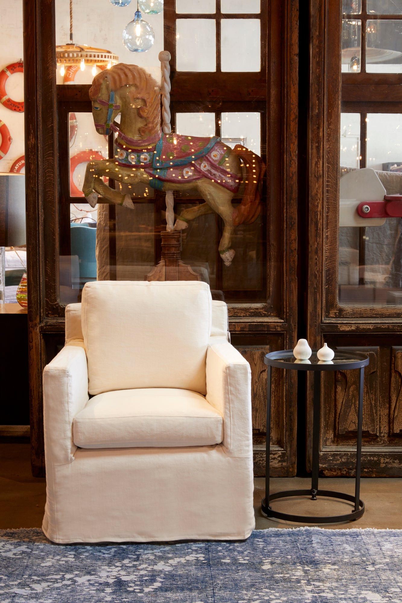  在Mariet Ivory的路易迷你椅子旁边的金属边桌. 背景是一个棕色的柜子，里面有一匹旋转木马作为装饰. 