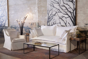  露西的椅子在奥的斯白色旁边的一个轻沙发，金属落地灯，和玻璃咖啡桌. 背景是一面混凝土墙，墙上挂着一幅巨画. Photographed in Otis White 
