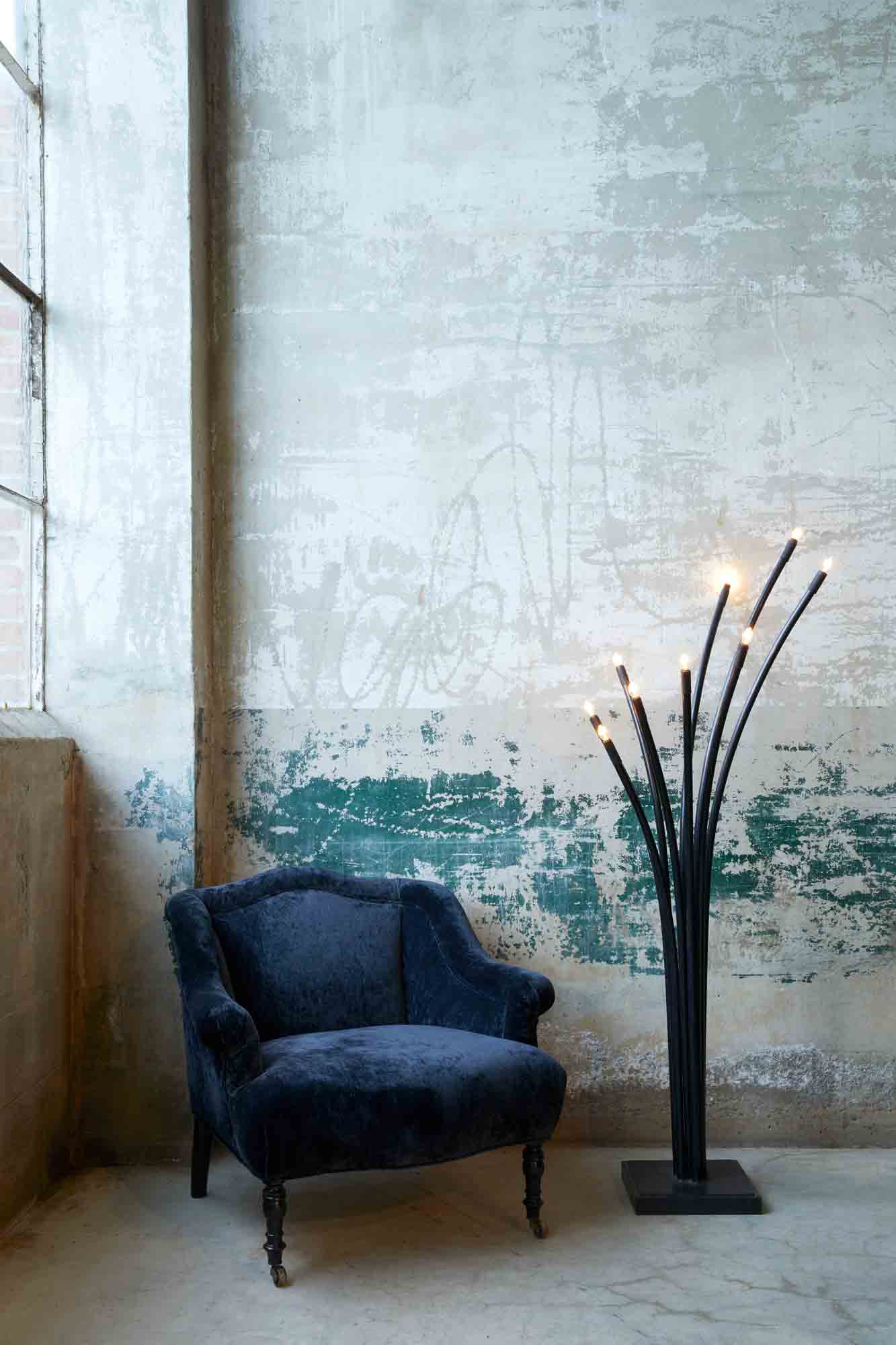  深蓝色织物的软垫椅，旁边是ramo落地灯 , 它们都靠在破旧的砖墙和大窗户上.  