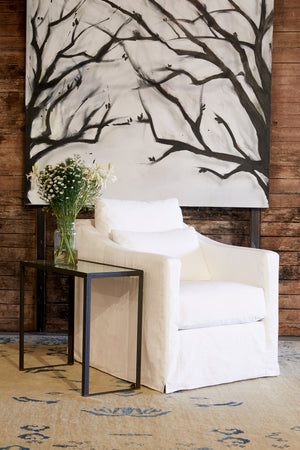  丽贝卡椅子在牛仔白旁边的金属边桌. 背景是画有树枝的木墙. 