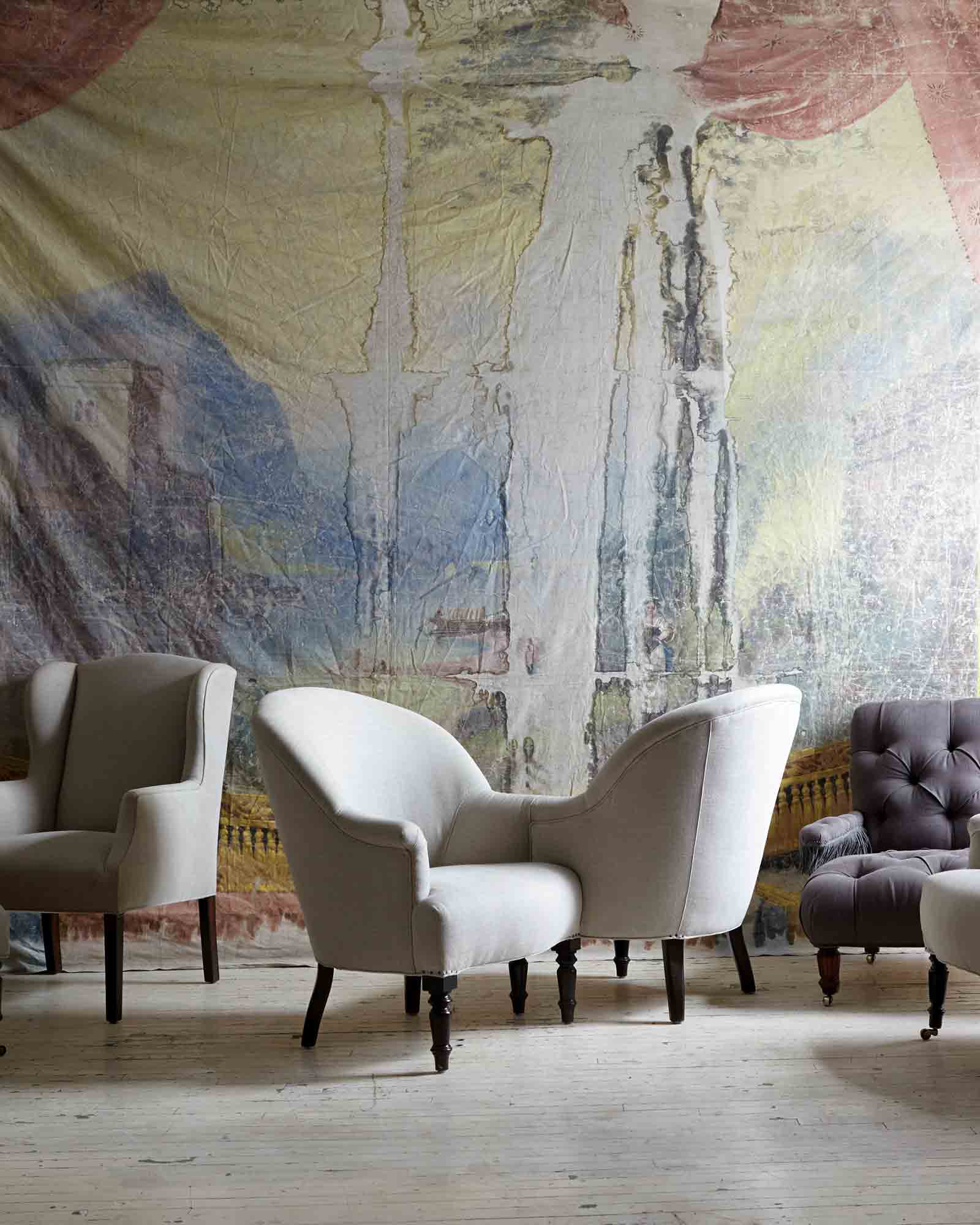  Tete-a-Tete椅子在复古亚麻旁边的各种椅子. 背景是一幅巨大的古董画，占据了整面墙. 