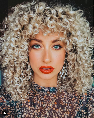 Woman with blonde curls and dark roots wearing red lipstick