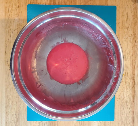 a pink paste in a mixing bowl on a blue cutting board and wooden table