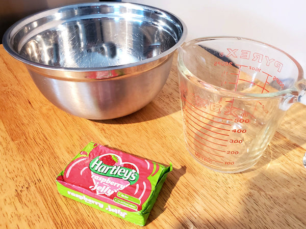 a measuring cup, a mixing bowl and Hartley's Raspberry Jelly on a wooden table