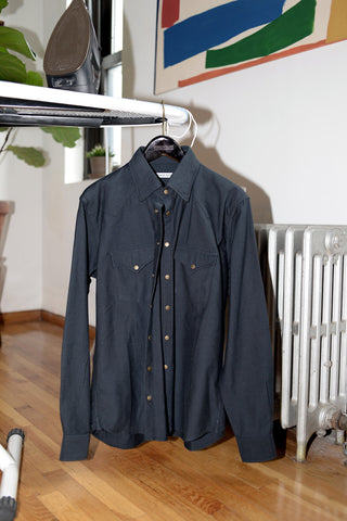 Black western shirt on a hanger balanced at the end of an ironing board.