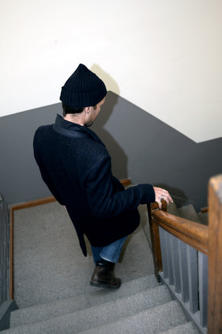 Dylan walks down the stairs wearing a wool overcoat and beanie.