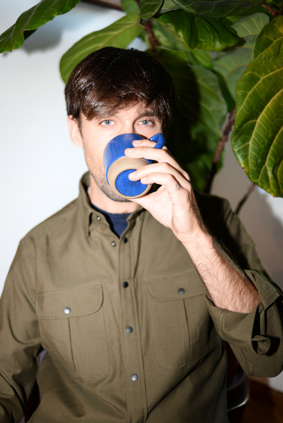 Dylan wears a green button down shirt and drinks from a mug.