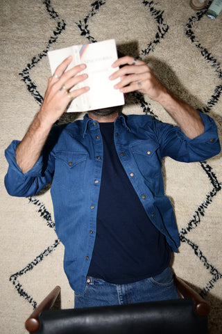 Dylan wears a chambray western shirt over a navy t-shirt. He is laying on a rug.