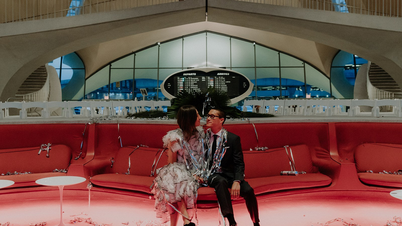Image of a bride and groom sitting at the TWA hotel in NYC covered with streamers.