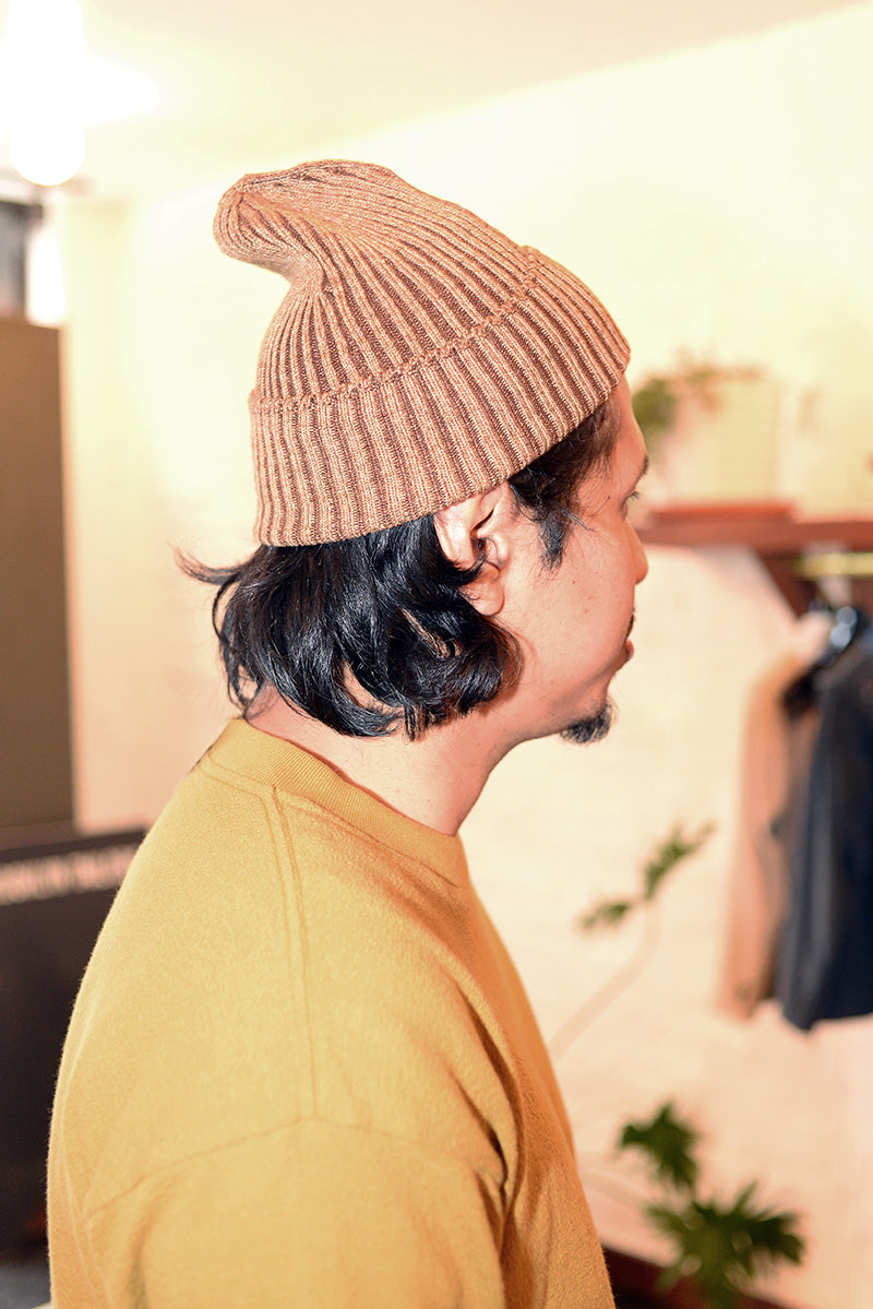 Close-up image of model wearing a brown beanie and ochre t-shirt. 