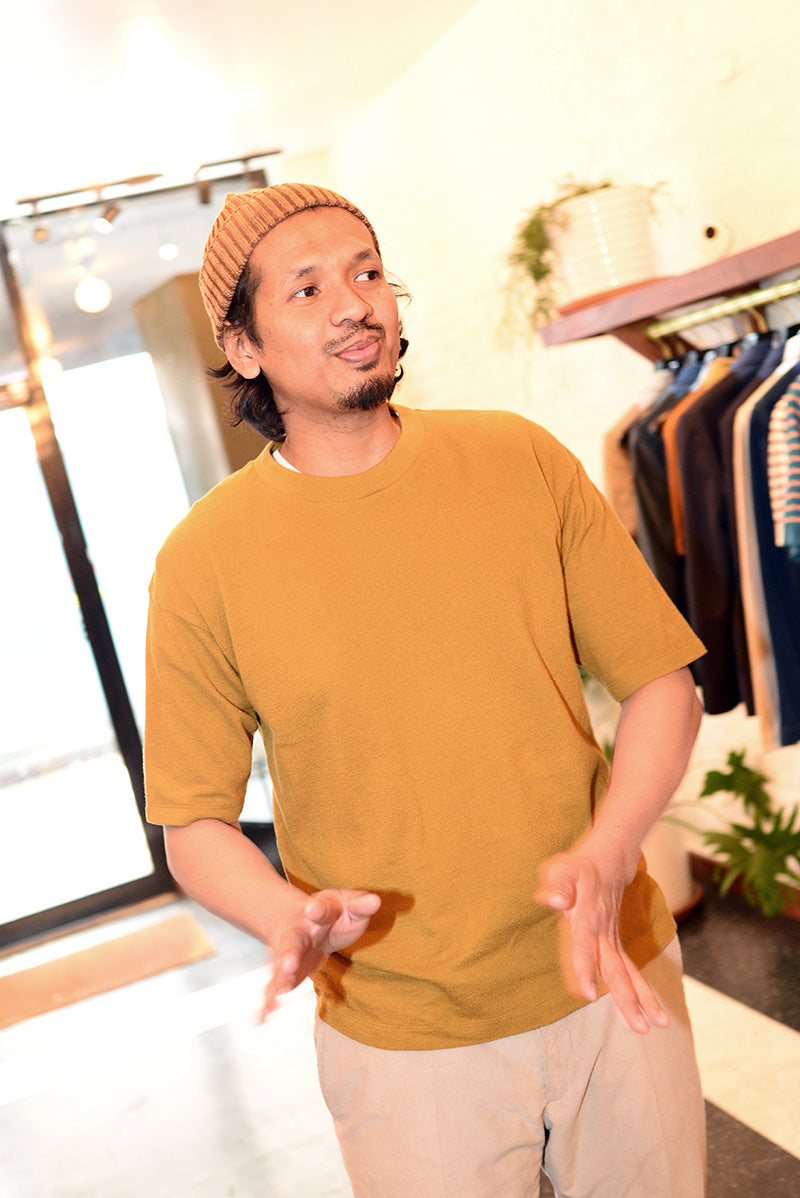 Front-facing image of mode wearing a brown beanie and ochre t-shirt in a clothing store. 