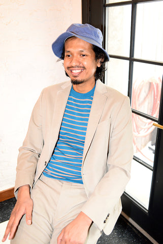 Supplemental shot of model wearing sand colored unstructured suit with blue and red striped t-shirt and bucket hat. 